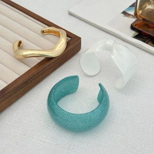 Dettaglio di bracciali dorati ondulati e rigidi in resina con fiocco e glitter