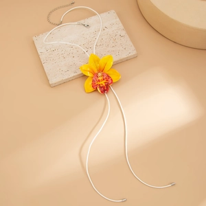 Detailed view of a yellow orchid flower pendant on a white cord necklace with natural light