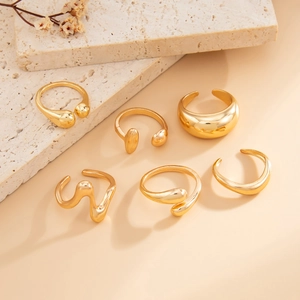 Detailed close-up of six gold minimalist open rings on a textured stone surface