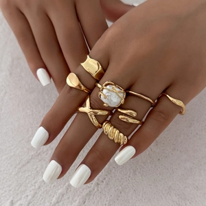 Close-up of seven irregular gold rings with Baroque pearl on a textured background