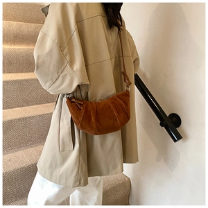 Détail du sac croissant caramel avec plis texturés et finition suède sur manteau beige