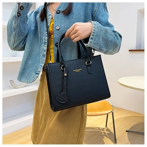 Detail of black quilted tote bag with gold logo lettering and heart-shaped leather charm