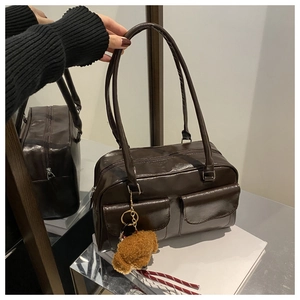 Détail d'un sac à bandoulière vintage marron foncé avec poches frontales et pendentif ours