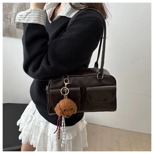 Detalle de bolso bandolera marrón con bolsillos delanteros y colgante de caniche de peluche