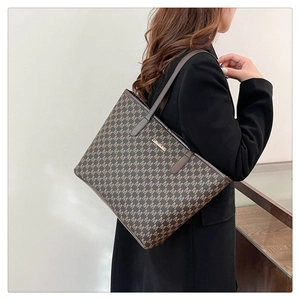 Detail view of large brown tote bag featuring classic M-letter print and metal logo plate