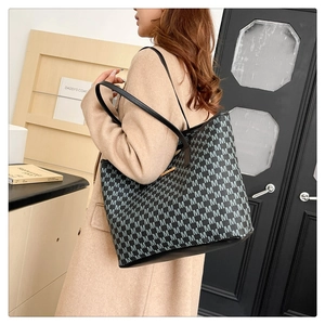 Détail du motif monogramme et logo en métal doré sur un sac cabas noir et blanc