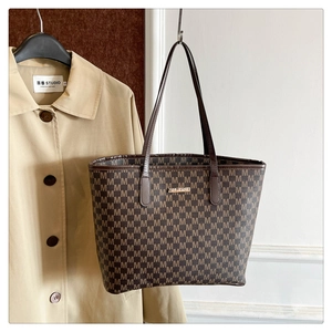 Détail d'un sac cabas marron avec imprimés de lettres et logo doré à côté d'un manteau