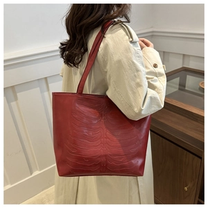 Detail of dark red crocodile bone embossed tote bag worn with a light trench coat