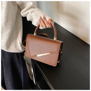 Detail of brown lychee grain leather crossbody bag with elegant gold metal bar accent