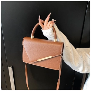 Detailed view of brown lychee grain leather handbag with gold metal bar and top handle