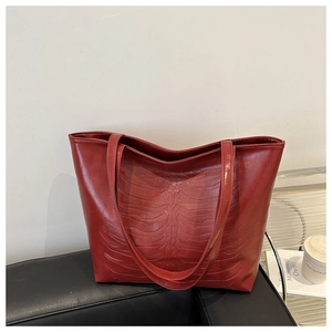 Detailed view of burgundy tote bag with unique bone relief pattern on black leather sofa