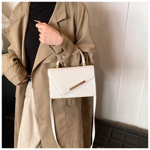 White lychee grain crossbody bag with gold metal trim styled on a trench coat