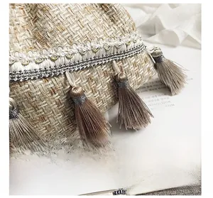 Dettaglio della trama in tweed beige con frange e pizzo delicato su una borsa a secchiello