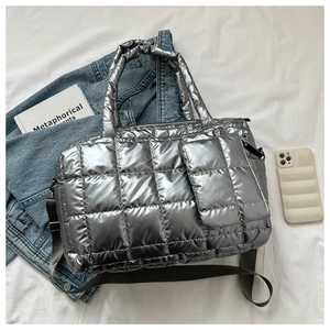 Détail du sac cabas matelassé argenté avec bandoulière réglable sur un tissu blanc