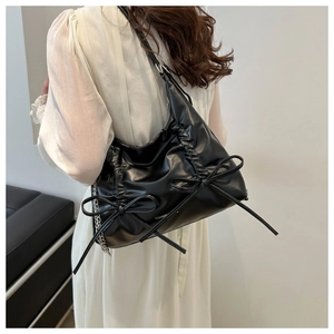 Detail of black pleated shoulder bag with bow decoration and silver metal chain strap