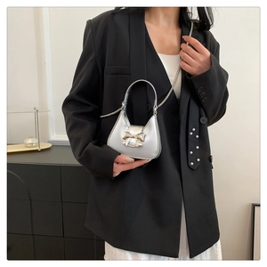 Detail of silver metallic mini handbag with bow accent and chain strap worn on black suit