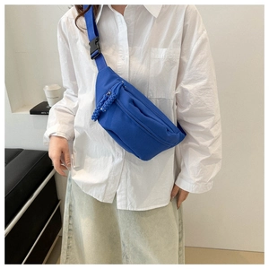 Close-up of blue canvas chest bag with woven zipper pull and black plastic buckle strap