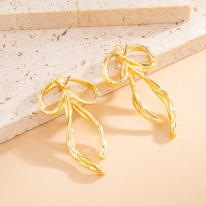 Detail showing fluid irregular gold bow earrings with a glossy metallic finish on a stone pedestal