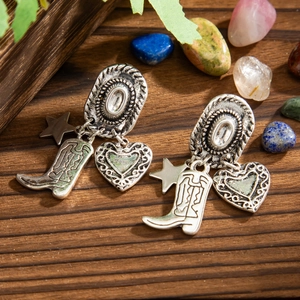 Macro detail of vintage silver cowboy hat earrings with star and boot charms on wood