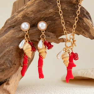 Detalle de conjunto de joyas oceánicas con coral rojo y conchas sobre madera