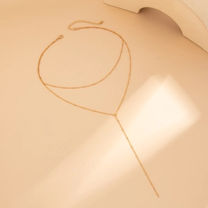 Dettaglio della collana a Y a doppio strato dorata con perle di metallo su sfondo caldo