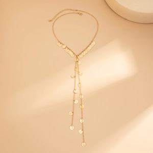 Dettaglio di una lunga collana a Y dorata con monete metalliche e catena regolabile su beige