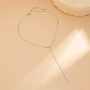 Vista dettagliata della collana a Y argento con piccoli cristalli su sfondo beige