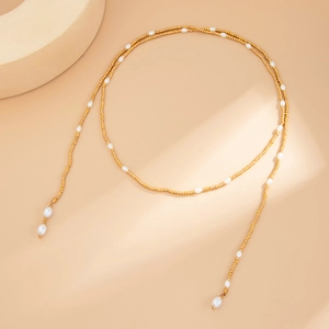 Dettaglio di una collana lunga con perline dorate e perle bianche eleganti da donna