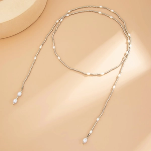 Dettaglio di una collana lunga con perline argentate e perle bianche irregolari