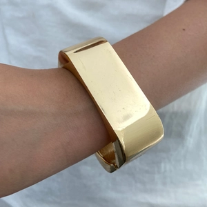 Dettaglio dell'ampio bracciale rigido dorato geometrico irregolare indossato al polso