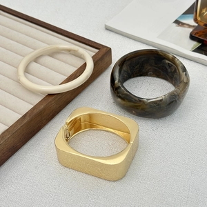 Vista macro di bracciali geometrici in resina e metallo dorato su espositore in legno