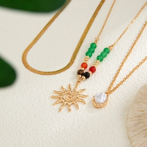 Close-up of layered gold necklaces with sun pendant and baroque pearl on stone