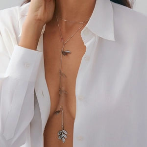 Dettaglio di una collana a Y argento con ciondoli a foglia di cristallo su camicia bianca