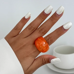 Nahaufnahme eines klobigen orangefarbenen Harzrings mit Marmorstruktur auf der Hand