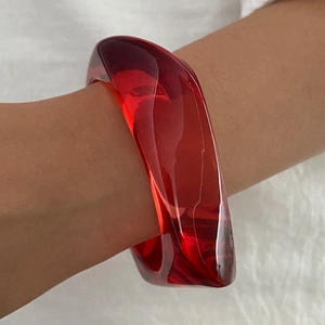 Dettaglio macro di un ampio bracciale in resina rossa traslucida con curve irregolari