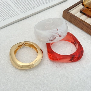 Dettaglio di bracciali in resina marmorizzata, rosso trasparente e fascia in metallo dorato