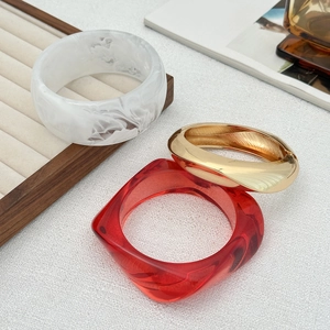 Dettaglio di bracciali spessi in resina e metallo dorato su sfondo bianco materico