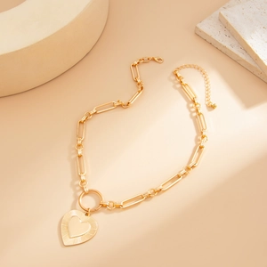 Macro shot of gold-plated lava heart pendant and chunky paperclip chain on stone tray