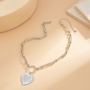Macro detail of silver heart pendant with textured finish on a paperclip chain necklace