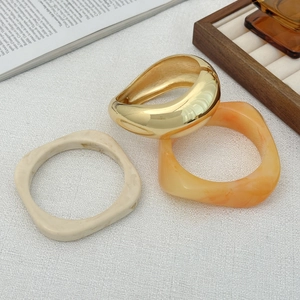Dettaglio di un set di bracciali geometrici in resina e metallo dorato su trama