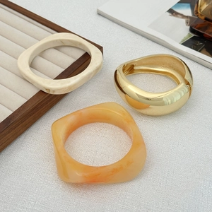 Vista macro di braccialetti geometrici in resina e polsino dorato su una rivista