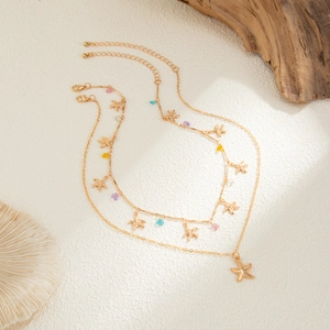 Dettaglio della collana dorata a strati con stelle marine e perline colorate su corallo