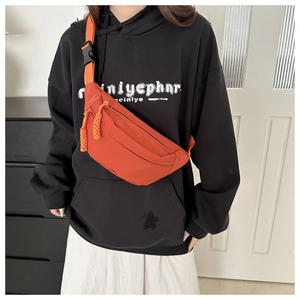 Detail view of a trendy orange nylon crossbody chest bag worn by a model in a home setting