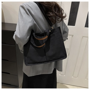 Détail du grand sac cabas en toile noire avec anses en cuir marron porté par un mannequin