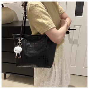 Dettaglio di borsa tote nera pied-de-poule con ciondolo in peluche bianco e inserto in pelle