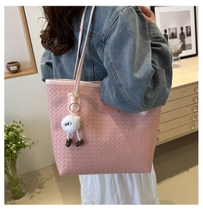 Détail d'un sac cabas tissé rose avec un charm en peluche blanc et écusson logo