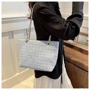 Détail d'un sac cabas bleu clair en tissu à carreaux avec franges et bandoulière dorée