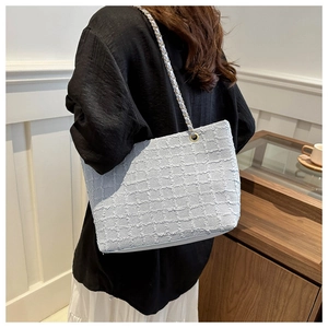 Detail of light blue textured tote bag with metal chain strap worn by a female model