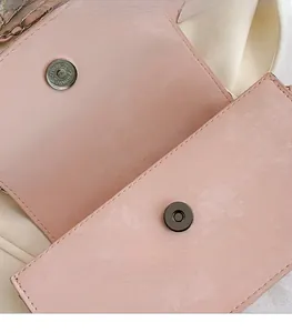 Makro-Detail der goldenen Magnetschnalle an einer rosa Ledertasche mit Kreuzmaserung
