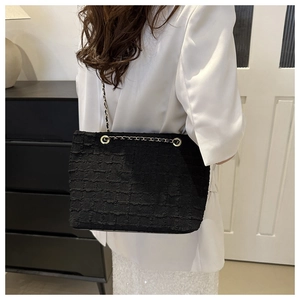 Detail of black tweed shoulder bag with woven texture and gold chain strap on model